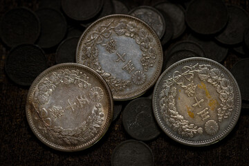 Close-up photo of the reverse side of Meiji era Japanese 50 sen silver coins arranged in a pile on a dark wooden surface. © Mr