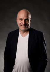 Fototapeta premium Bald man smiling, wearing dark blazer and white t shirt for a studio portrait