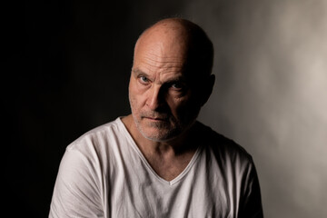 Fototapeta premium Older man's portrait with baldness, a serious expression, and stark dramatic lighting