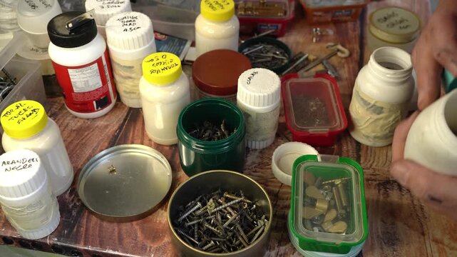 Man arranging screws, nails, nuts and other items in different boxes, jars and cans.