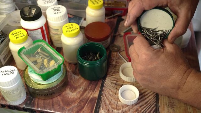 Man arranging screws, nails, nuts and other items in different boxes, jars and cans.