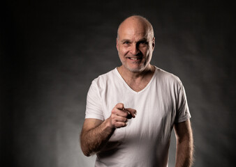 Naklejka premium Confident senior man choosing or motivating, wearing white t shirt on dark background