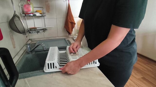 A woman cleans a plastic dish dryer at the kitchen sink - home cleaning, hygiene, care of kitchen accessories.
