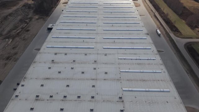 Aerial Warehouse Roof Rows Skylights Showing Maintenance Crew And Service Truck, Calm Industrial Morning, Drone Inspection Capturing Vents And Access Hatches, Concrete Apron And Surrounding