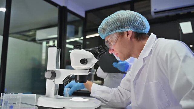 Professional male and female scientists in protective gear working with microscope in modern laboratory