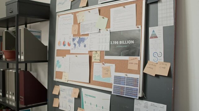 Close up no people shot of office workspace with corkboard covered with documents and sticky notes near bookshelf with folders