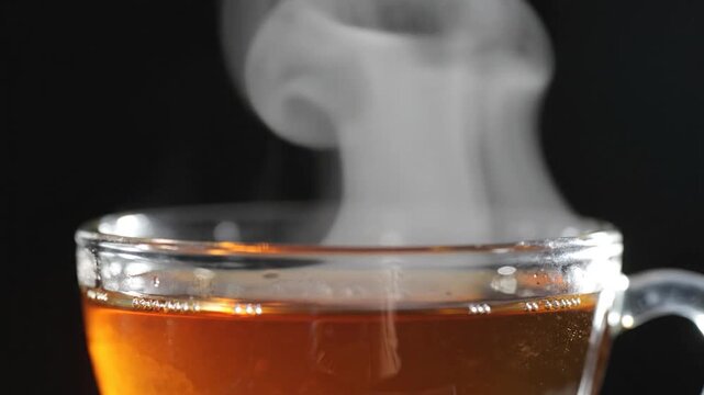 Close-up of hot tea steaming in a clear glass mug against a dark background.