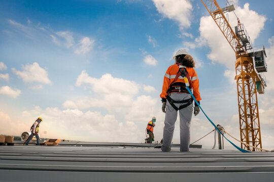 Construction worker wearing safety harness and safety line working on a metal industry roof new warehouse