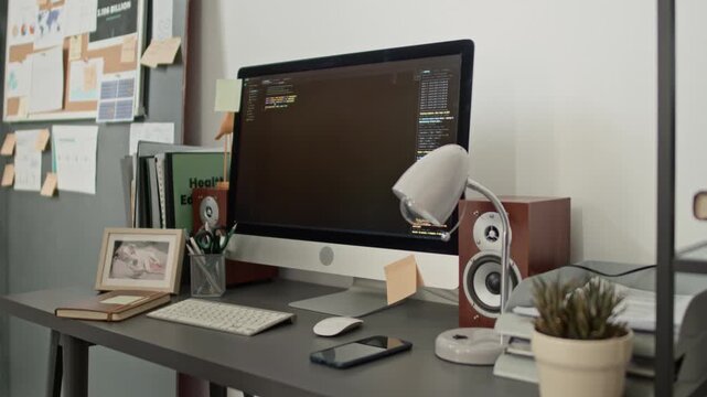 No people shot of desk with monitor displaying open-source code, and cluttered with office supplies, books, and notes on whiteboard