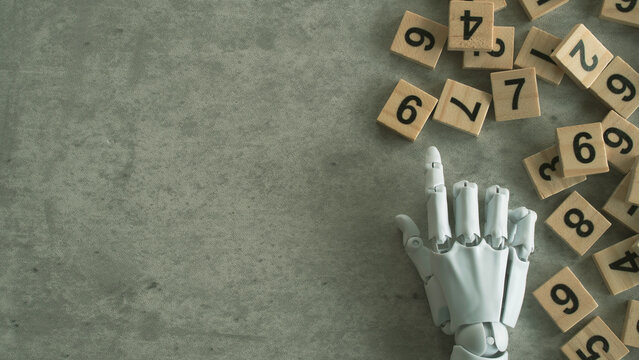 A white bionic hand interacting with a pile of wooden number blocks on a concrete background.