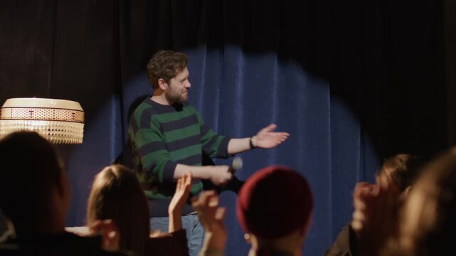 Cheerful host introducing and greeting female standup performer on stage in front of applauding audience, she taking microphone and beginning her monologue at comedy event