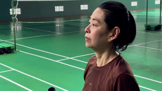 Athletic Young Woman Hydrating with Large Water Bottle on Indoor Badminton Court After Workout
