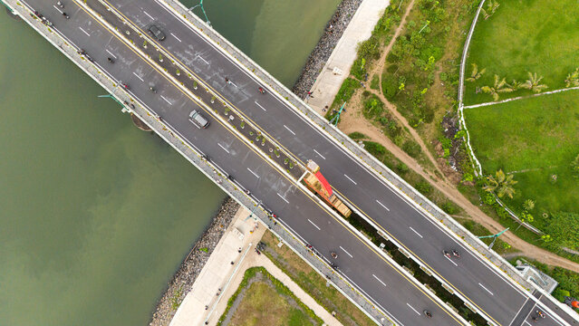 A stunning aerial view of Kretek 2 Bridge, showcasing smooth traffic flow over the river, connecting two sides of the lush green landscape in Yogyakarta.
