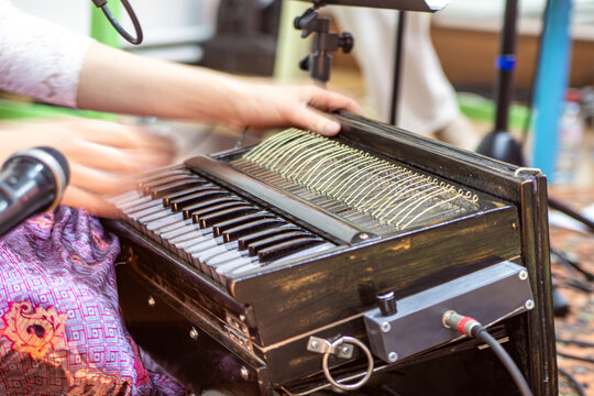 Person plays old wooden harmonium with shiny keys and wires while singing into mic at cozy jam session