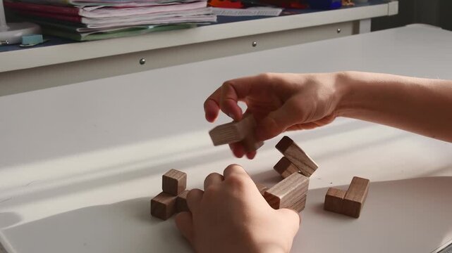 Close-up of hands solving a wooden 3D logic puzzle on a white desk. Concept for problem-solving and strategy
