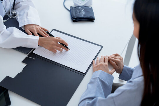 Doctor explaining treatment plan and obtaining informed consent while patient signing consent form in hospital.