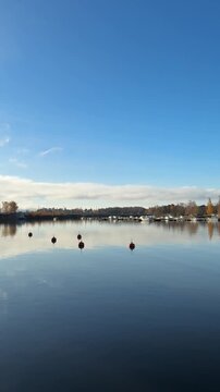 Peaceful lakeside boardwalk at Lake Zurich in Horgen Switzerland with still water reflections, autumn trees and soft clouds under blue sky, serene natural scene