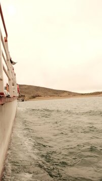 View from moving boat across lake near dry hills in Sajama National Park Bolivia, gentle waves and remote natural landscape under soft hazy sky, calm travel scene