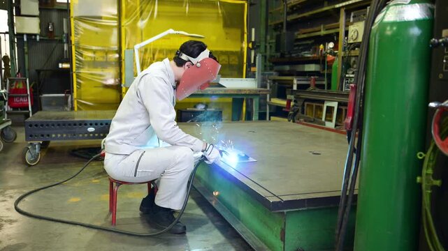 製造業の工場でアーク溶接作業を行う溶接ヘルメットをつけた作業員のものづくり現場と技術の動画スローモーション