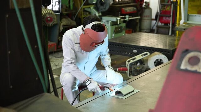 製造業の工場で火花散るアーク溶接作業を行う溶接ヘルメットをつけた作業員のものづくり現場と技術の動画全身