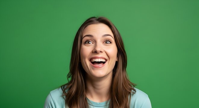 Young woman s happy surprised expression showing teeth with wide open mouth and eyes looking up against a saturated green color backdrop conveying genuine joy and sudden astonishment in a