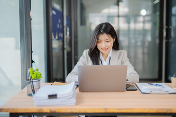 Fototapeta premium Asian businesswoman doing financial market research using laptop and digital tablet on digital investment in front of modern office.