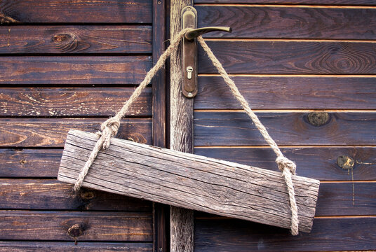 An old wooden board made of cracked wood with empty space for text hangs on ropes on door