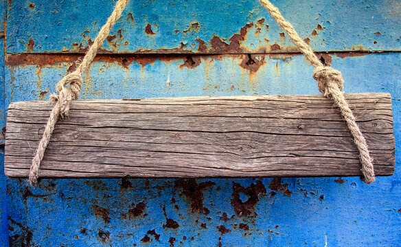 An old wooden board made of cracked wood with empty space for text hangs on ropes on door