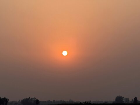 Serene orange sunset creating a hazy atmosphere across the vast sky with a small bright sun