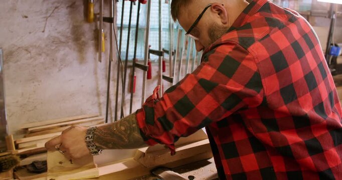 Woodworking process. Jointer planer. Carpenter male hand pushing long plank on professional electric equipment with sawdust on benchtop.
