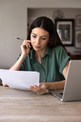 Focused adult woman sits at desk, reading documents text, analyzing details, reviewing information of contract terms data, learning insurance papers, doing remote work from home office, vertical shot © fizkes