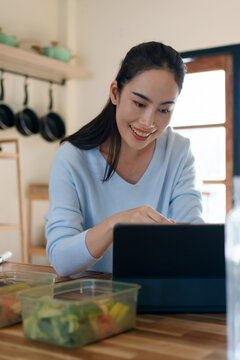 Woman using tablet to follow healthy cooking recipe while preparing fresh meal at home kitchen