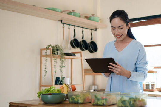 Woman using tablet to follow healthy cooking recipe while preparing fresh meal at home kitchen