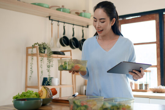 Woman using tablet to follow healthy cooking recipe while preparing fresh meal at home kitchen