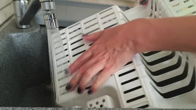 Close-up - a plastic dish dryer is rinsed under the faucet in the kitchen, cleaning, hygiene, cleanliness, home care.
