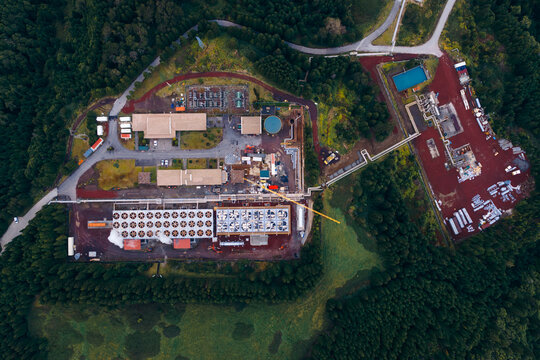 Aerial view of the Ribeira Grande Geothermal Power Station with its industrial buildings and cooling towers surrounded by lush green forests in Ribeira Grande, Acores, Portugal.