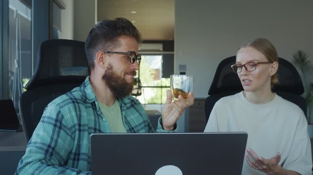 Two technical writer enjoying relaxing tea break in modern office, sitting in comfortable chairs, using laptop, and engaging in conversation. technical writer think about new text for project