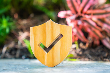 Fototapeta premium Wooden shield icon with checkmark symbol in garden. Data protection, security guarantee, insurance policy, and privacy safety concept for business and environment technology.