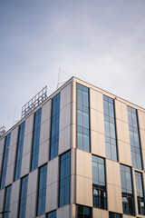 Fototapeta premium The geometric corner of a modern office building features sleek white panels and large glass windows. This low-angle perspective highlights contemporary urban architectural design.