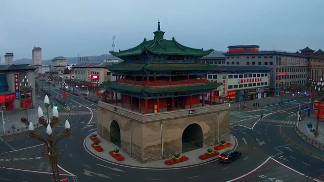 The majestic ancient Drum Tower of Linfen stands at the heart of a modern urban traffic circle under a clear sky.