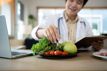 Fototapeta premium Male dietitian sitting at desk with different healthy products and writing diet plan, Healthy life style concept, doctor writing, diet and losing weight