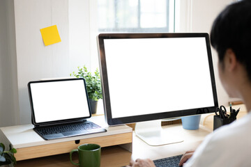Fototapeta premium Shoulder to back view. young man using computer and tablet at workplace close up view of white screen. mock up banner for website header design with copy space for text