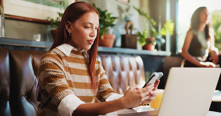 Fototapeta premium Woman, phone and laptop in restaurant with remote work, email and social media marketing notification. Freelancer, person and typing in cafe with tech, mobile app and website for online advertising.