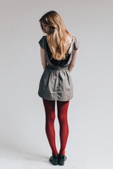 Fototapeta premium Young Woman In Grey Dress And Red Stockings Standing Against A White Background