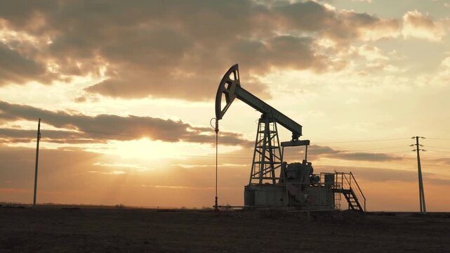 Oil pump jack working at sunset, extracting crude oil from the ground.