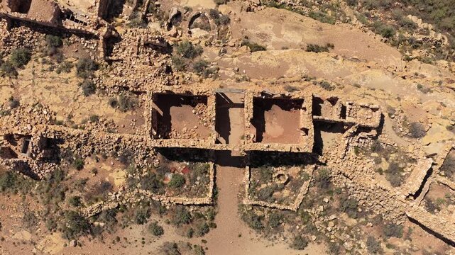 A top down drone view reveals the geometric patterns of abandoned stone ruins in the Southwest. The weathered walls and roofless structures sit in stark contrast to the arid desert floor.