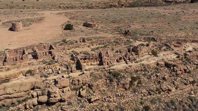 A cinematic drone view explores abandoned stone ruins from the cowboy era. These historical structures sit on the edge of a rugged southwest desert canyon, showcasing the decay of the Old West.