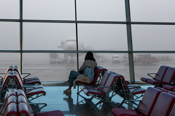 A lonely woman waiting for her delayed flight in foggy weather in the Airport - Busy airport airfield runway with group of airplanes queueing to departure heavy air traffic - istanbul airport, istanbu © muratart