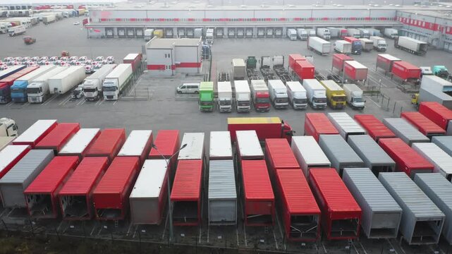 Aerial Drone View of Large Logistics Complex with Rows of Red and White Truck Trailers, Loading Docks and Warehouse | Freight Distribution Hub Overhead Shot