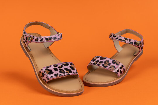 Stylish leopard print sandals with on orange background. Trendy summer footwear for women or girls. Fashionable flat shoes for vacation and casual wear.